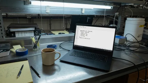 Laptop on a lab bench showing a JSON config file next to a closed terminal, cool overhead light, no logos